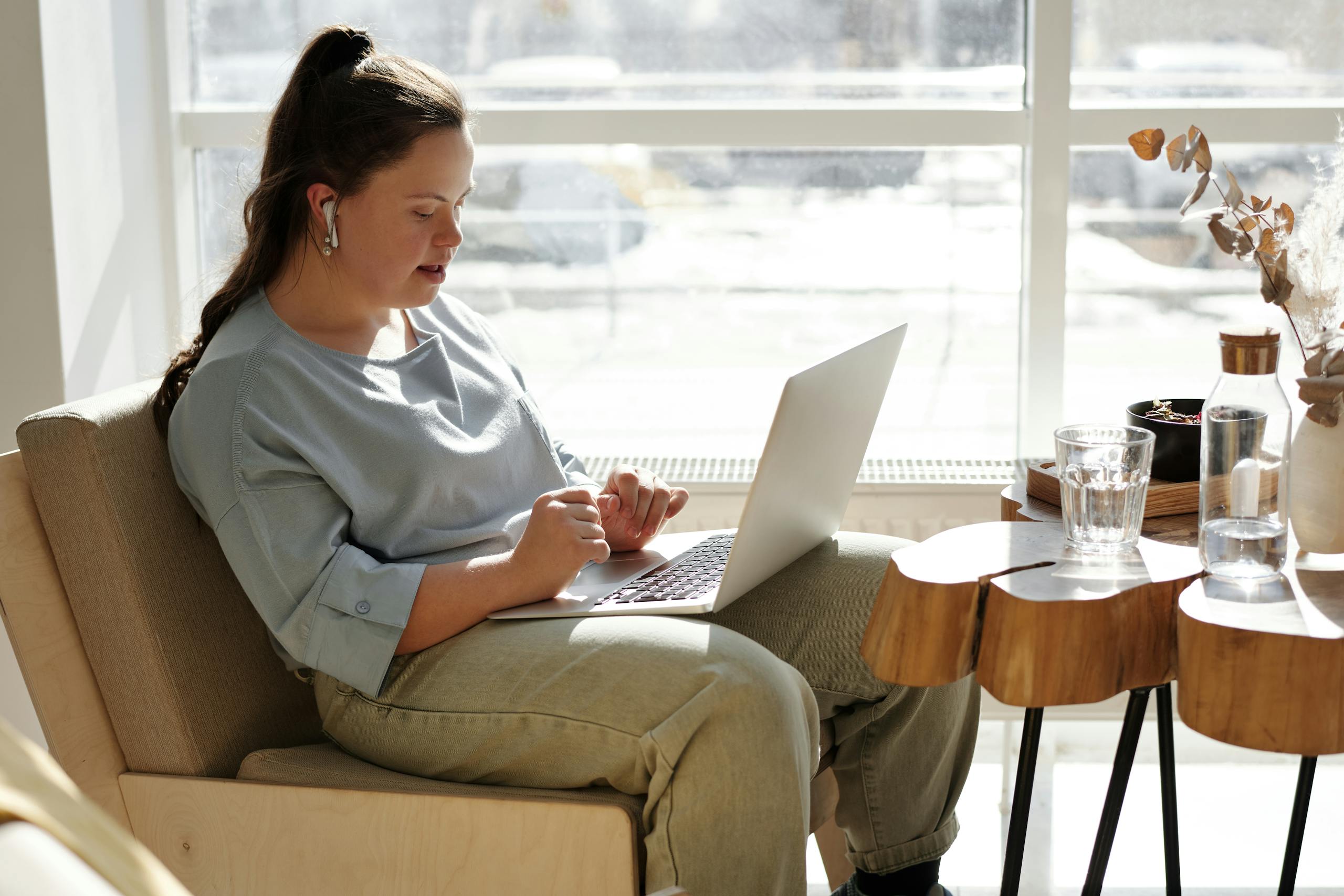 Young woman with Down syndrome using a laptop at home in a bright, cozy space.